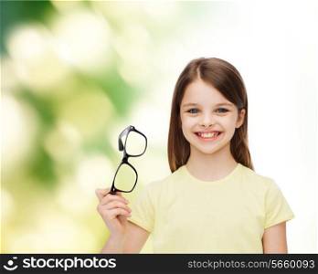 education, school and vision concept - smiling cute little girl holding black eyeglasses