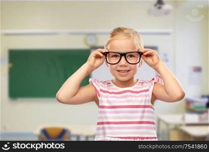 education, school and vision concept - smiling cute little girl in black glasses over classroom background. smiling cute little girl in black glasses