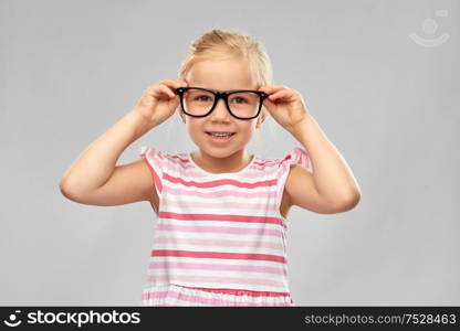 education, school and vision concept - smiling cute little girl in black glasses over grey background. smiling cute little girl in black glasses