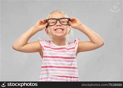 education, school and vision concept - smiling cute little girl in black glasses over grey background. smiling cute little girl in black glasses