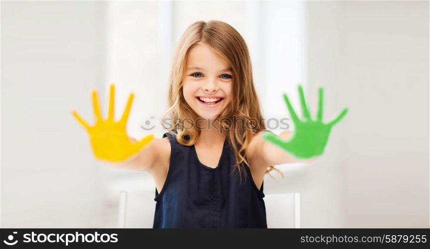 education, school, art and happiness concept - little student girl showing hands in yellow and green color at school