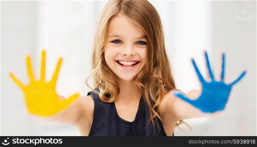 education, school, art and happiness concept - little student girl showing hands in yellow and blue color at school