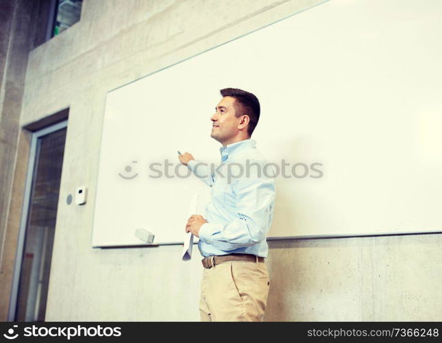 education, school, business, teaching and people concept - happy teacher or businessman pointing marker to white board at lecture. teacher pointing marker to white board at lecture