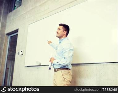 education, school, business, teaching and people concept - happy teacher or businessman pointing marker to white board at lecture. teacher pointing marker to white board at lecture