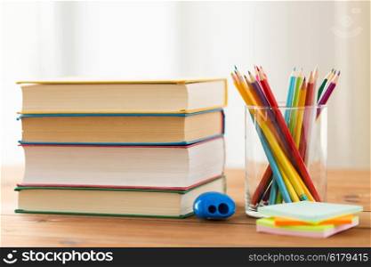 education, school, creativity and object concept - close up of crayons or color pencils with books, stickers and sharpener on wooden table