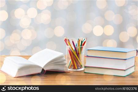 education, school, creativity and object concept - close up of crayons or color pencils and books on wooden table over holidays lights background