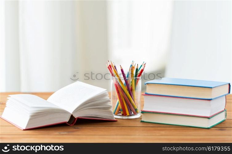 education, school, drawing, creativity and object concept - close up of crayons or color pencils and books on wooden table