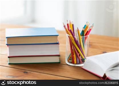 education, school, drawing, creativity and object concept - close up of crayons or color pencils and books on wooden table