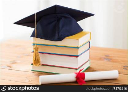 education, school, graduation and knowledge concept - close up of books and mortarboard with diploma on wooden table