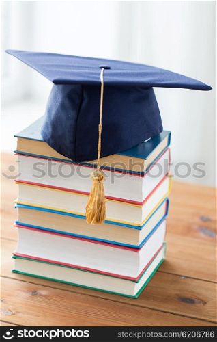 education, school, graduation and knowledge concept - close up of books and mortarboard on wooden table