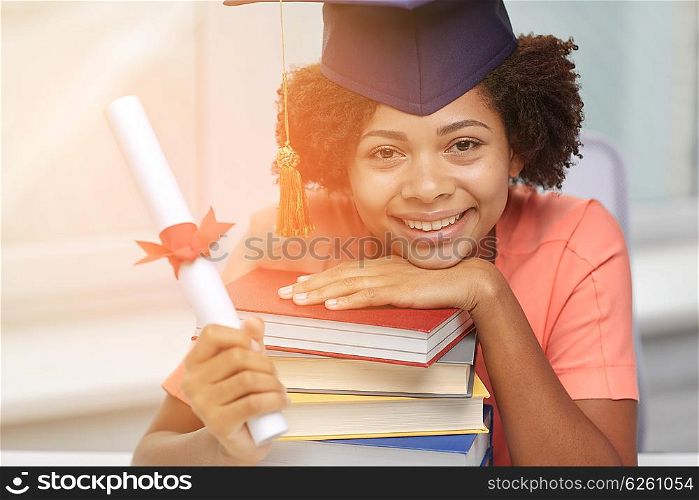 education, school, graduation and people concept - happy smiling african american student girl in bachelor cap with books and diploma sitting at table at home