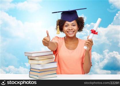 education, school, graduation, gesture and people concept - happy smiling african american student girl in bachelor cap with books and diploma showing thumbs up over blue sky and clouds background