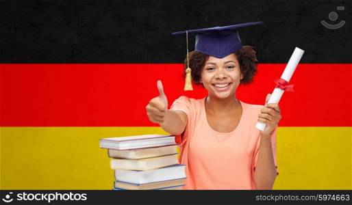 education, school, graduation, gesture and people concept - happy smiling african american student girl in bachelor cap with books and diploma showing thumbs up over german flag background