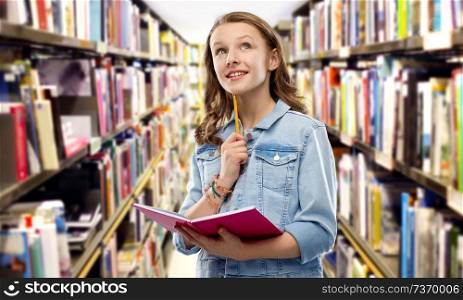 education, school, inspiration and people concept - teenage student girl in denim jacket with diary or notebook and pencil thinking over library background. student girl with diary or notebook at library