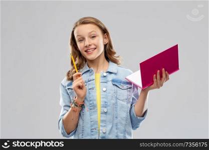 education, school, inspiration and people concept - young woman or teenage student girl in denim jacket with diary or notebook and pencil over grey background. teenage student girl with diary or notebook
