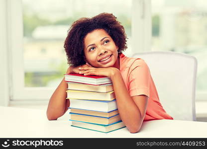 education, school, knowledge and people concept - happy smiling african american student girl with books sitting at table and dreaming at home