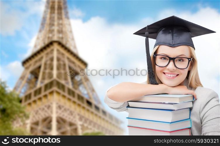 education, school, knowledge and people concept - picture of happy student girl or woman in trencher cap with stack of books over paris eiffel tower background