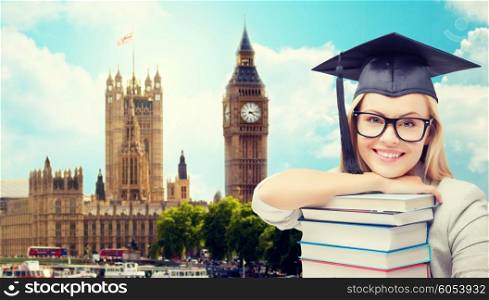 education, school, knowledge and people concept - picture of happy student girl or woman in trencher cap with stack of books over houses of parliament in london city background