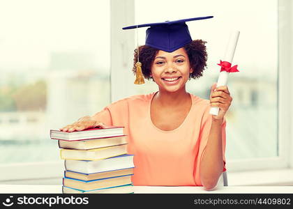 education, school, knowledge, graduation and people concept - happy smiling african american student girl in bachelor cap with books and diploma sitting at table at home