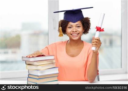 education, school, knowledge, graduation and people concept - happy smiling african american student girl in bachelor cap with books and diploma sitting at table at home