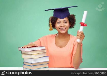 education, school, knowledge, graduation and people concept - happy smiling african american student girl in bachelor cap with books and diploma over green chalk board background