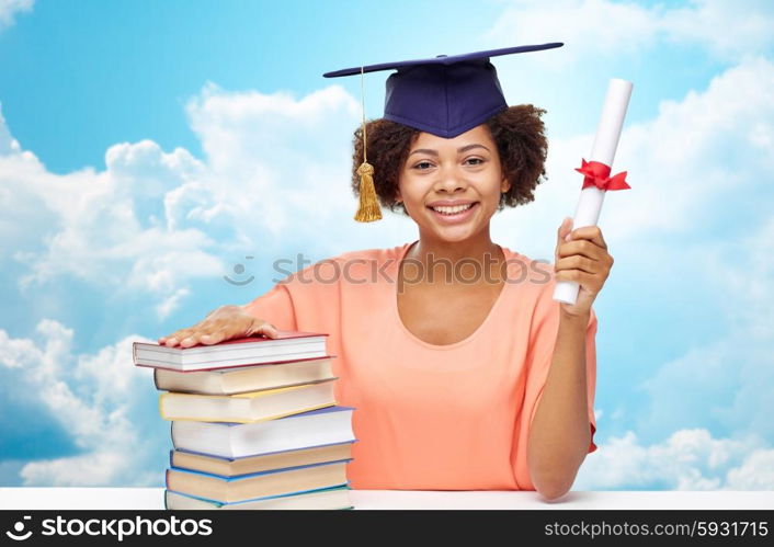 education, school, knowledge, graduation and people concept - happy smiling african american student girl in bachelor cap with books and diploma sitting at table over blue sky and clouds background