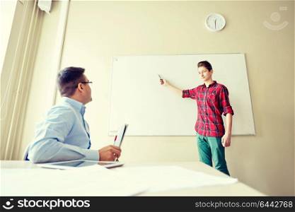 education, school, learning and people concept - student boy showing something on blank white board and teacher in classroom. student boy at school white board and teacher