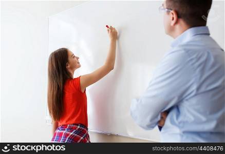education, school, learning and people concept - student girl writing something on blank white board and teacher in classroom