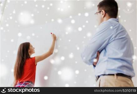 education, school, learning and people concept - student girl writing something on blank white board and teacher in classroom over snow. student writing on board and teacher at school