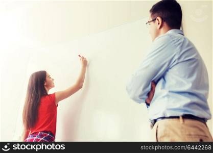 education, school, learning and people concept - student girl writing something on blank white board and teacher in classroom. student writing on board and teacher at school