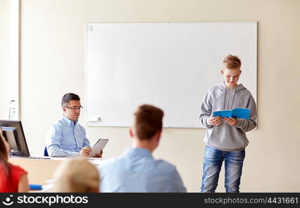 education, school, learning, examination and people concept - student boy with notebook and teacher in classroom