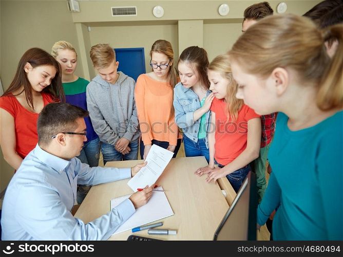 education, school, learning, teaching and people concept - group of students and teacher with tests in classroom