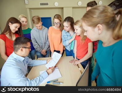 education, school, learning, teaching and people concept - group of students and teacher with tests in classroom