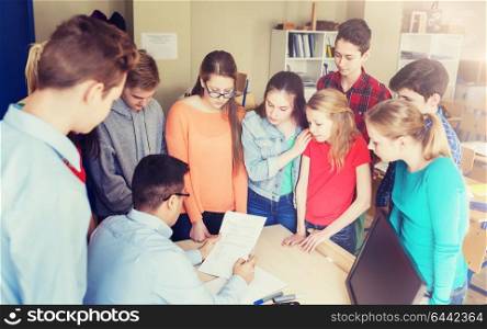education, school, learning, teaching and people concept - group of students and teacher checking tests at school. group of students and teacher with tests at school
