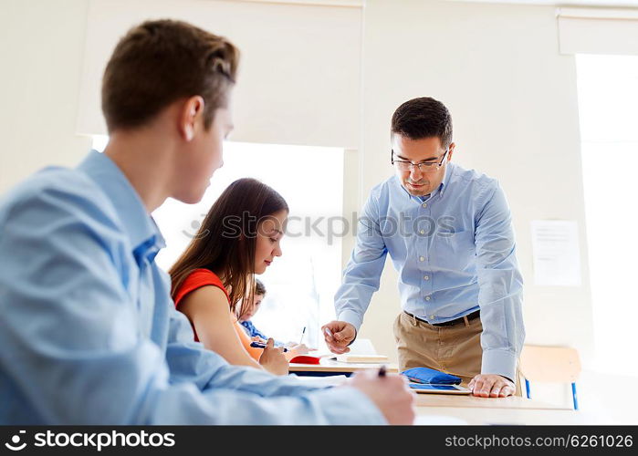 education, school, learning, teaching and people concept - group of students and teacher talking in classroom