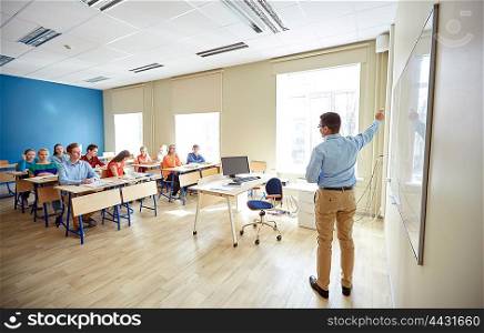 education, school, learning, teaching and people concept - teacher standing in front of students and showing something on white board in classroom