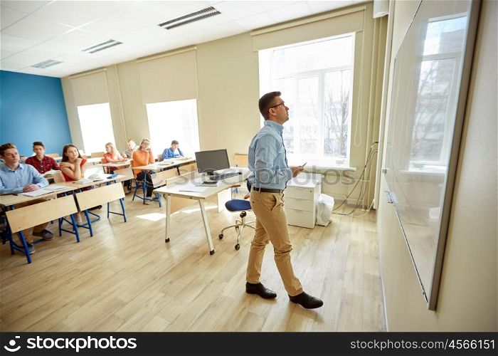 education, school, learning, teaching and people concept - teacher standing in front of students and writing something on white board in classroom