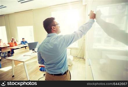 education, school, learning, teaching and people concept - teacher standing in front of students and writing something on white board in classroom. students and teacher writing on school white board