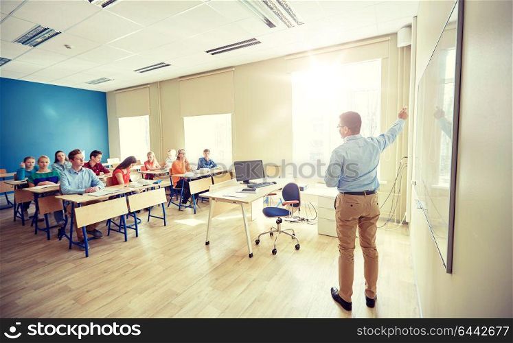 education, school, learning, teaching and people concept - teacher standing in front of students and showing something on white board in classroom. students and teacher at school white board