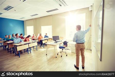 education, school, learning, teaching and people concept - teacher standing in front of students and showing something on white board in classroom. students and teacher at school white board