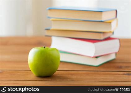 education, school, literature, reading and knowledge concept - close up of books and green apple on wooden table