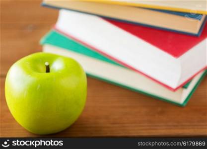 education, school, literature, reading and knowledge concept - close up of books and green apple on wooden table