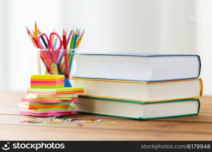 education, school supplies, and object concept - close up of stand or glass with writing tools and book with scissors on wooden table