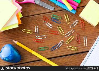 education, school supplies, stationery and object concept - close up of clips, pens and stickers on wooden table