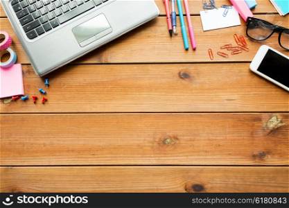 education, school supplies, technology and object concept - close up of stationery and laptop computer with smartphone on wooden table