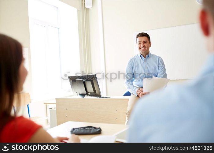 education, school, teaching, learning and people concept - group of happy students and teacher with papers or tests sitting on table