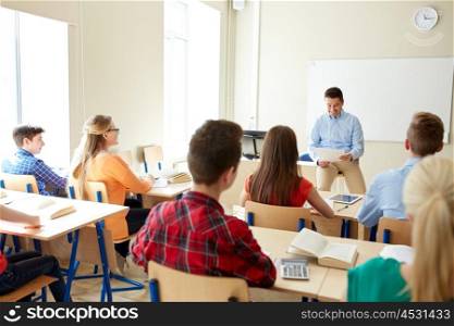 education, school, teaching, learning and people concept - group of happy students and teacher with papers or tests sitting on table. group of students and teacher with papers or tests
