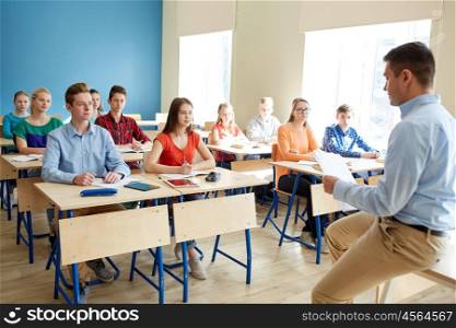 education, school, teaching, learning and people concept - group of students and teacher with papers or tests sitting on table