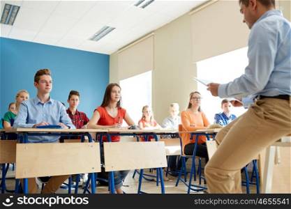 education, school, teaching, learning and people concept - group of students and teacher with papers or tests sitting on table
