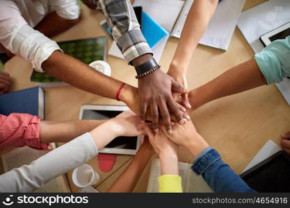 education, school, teamwork and people concept - close up of international students with hands on top of each other sitting at table